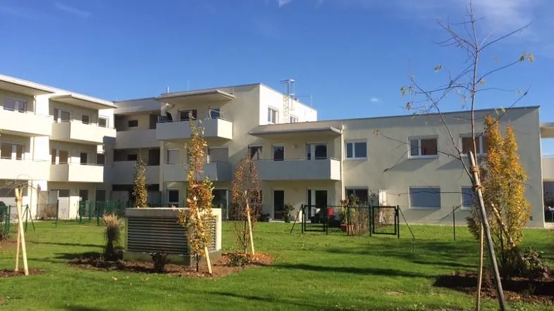 Modernes Mehrfamilienhaus mit gepflegter Grünfläche und Balkonen unter blauem Himmel.