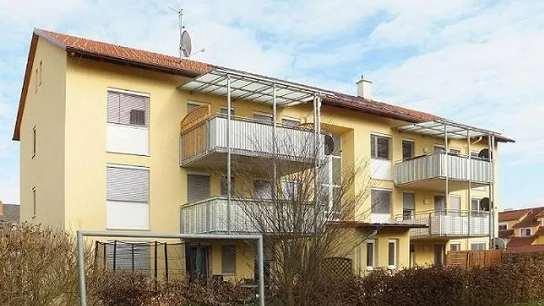 Gelbes Mehrfamilienhaus mit Balkonen, Rollläden und Satteldach in gepflegtem Zustand.