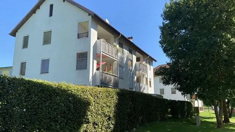 Weißes Mehrfamilienhaus mit Balkonen, umgeben von einer grünen Hecke und Rasenfläche.
