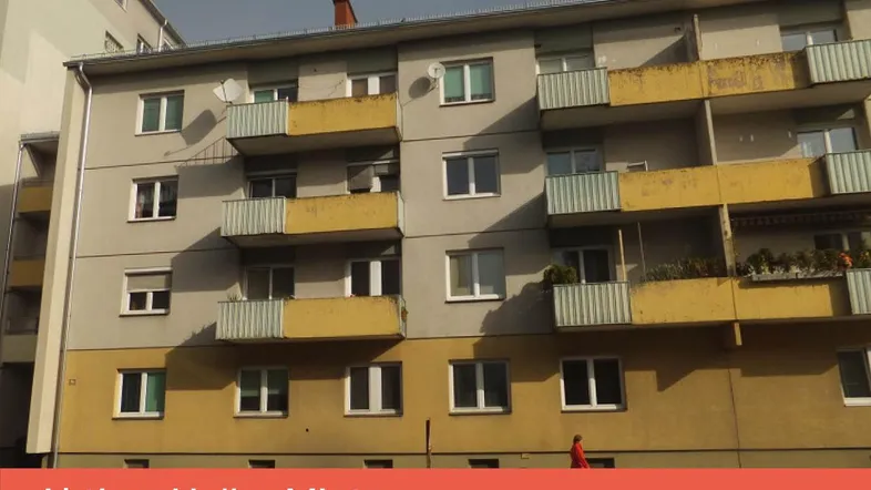 Mehrfamilienhaus mit gelben Balkonen und grauer Fassade unter bewölktem Himmel.
