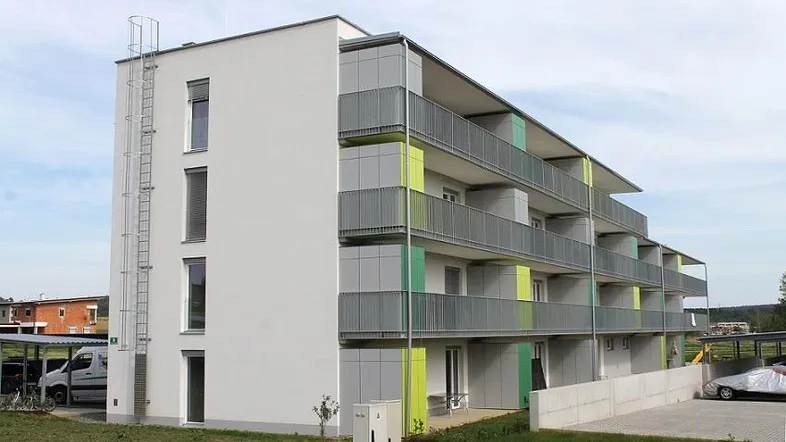 Modernes Mehrfamilienhaus mit weißer Fassade, farbigen Akzenten und Balkonen, ausgestattet mit einer Feuerleiter.
