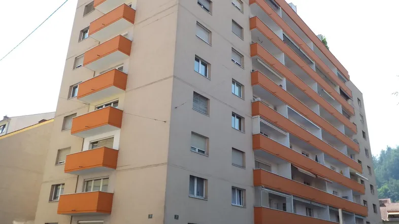 Mehrstöckiges Wohngebäude mit zahlreichen orangefarbenen Balkonen und heller Fassade in städtischer Umgebung.