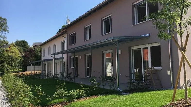 Moderne Reihenhäuser mit gepflegten Vorgärten und überdachten Terrassen unter blauem Himmel.