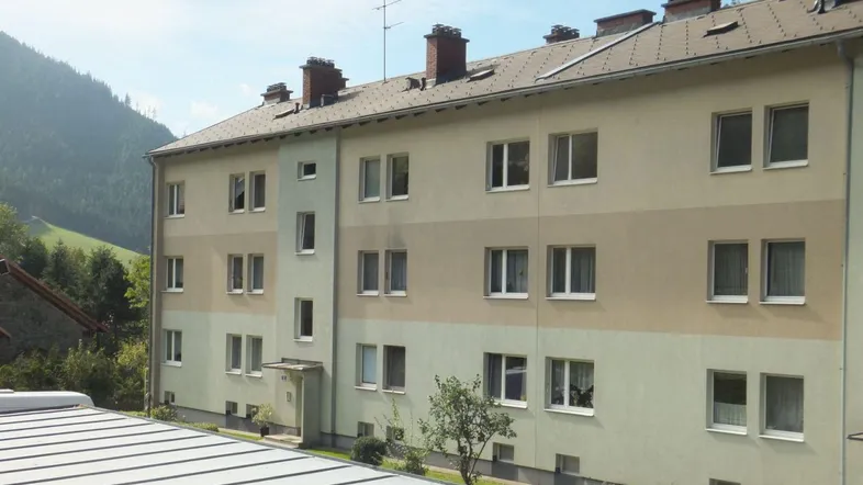Mehrfamilienhaus mit gestreifter Fassade, Satteldach und Bergblick in grüner Umgebung.
