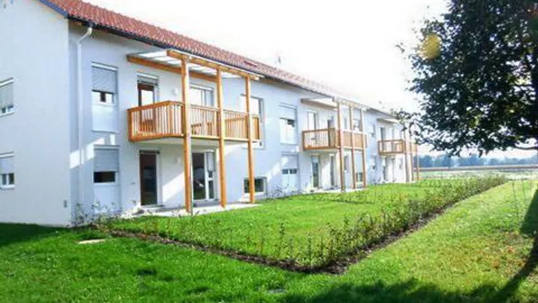 Modernes Mehrfamilienhaus mit weißer Fassade, Holzbalkonen und gepflegtem Rasenbereich.