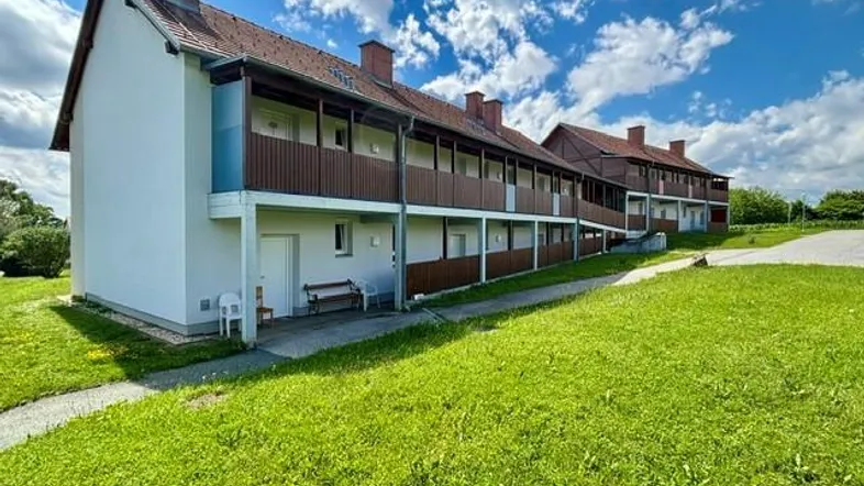 Mehrfamilienhaus mit mehreren Balkonen und großzügiger Grünfläche unter blauem Himmel.