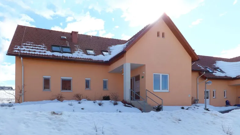 Einfamilienhaus mit oranger Fassade und Ziegeldach, umgeben von Schnee im Winter.