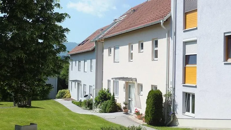 Mehrere moderne Reihenhäuser mit hellen Fassaden und gepflegten Grünflächen unter blauem Himmel.
