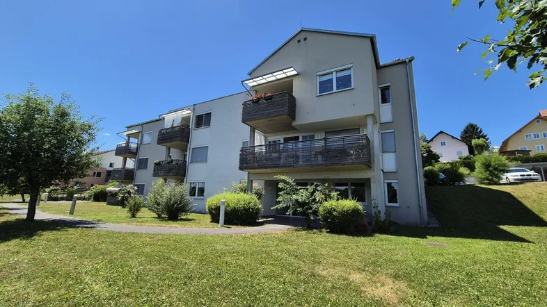 Modernes Mehrfamilienhaus mit Balkonen und gepflegter Grünfläche unter blauem Himmel.