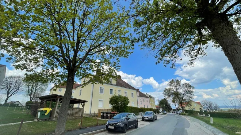 Blick auf die Straße mit geparkten Autos und einem Wohngebäude unter blauem Himmel.