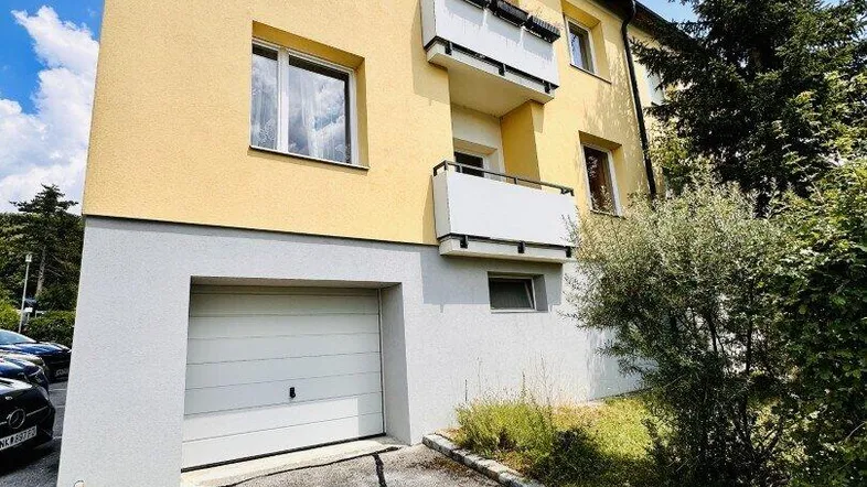 Gelbes Mehrfamilienhaus mit integrierter Garage und Balkonen unter blauem Himmel.