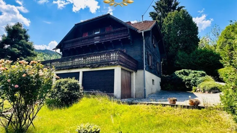 Traditionelles Holzhaus mit Balkon und großem Garten unter blauem Himmel.