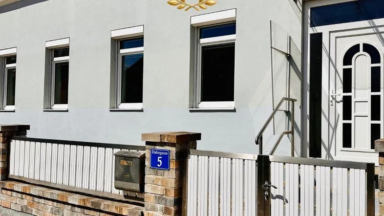 Graue Hausfassade mit weißen Fenstern und einem dekorativen Jubiläumslogo.