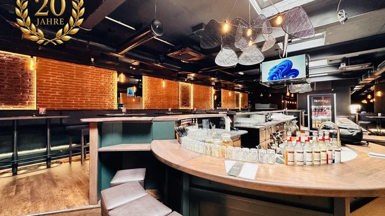 Moderne Bar mit Holztheke, freigelegten Ziegelwänden und stimmungsvoller Beleuchtung durch Oberlichter.