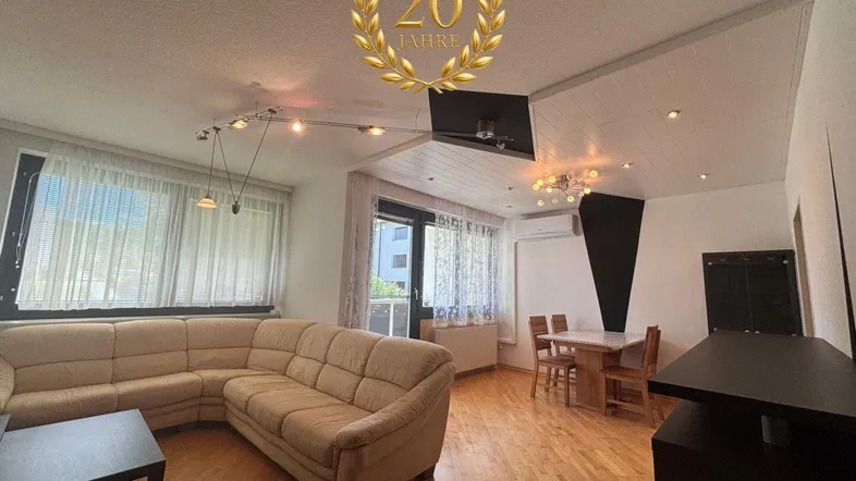 Heller Wohn- und Essbereich mit beigem Ecksofa, Holzboden und Zugang zum Balkon.