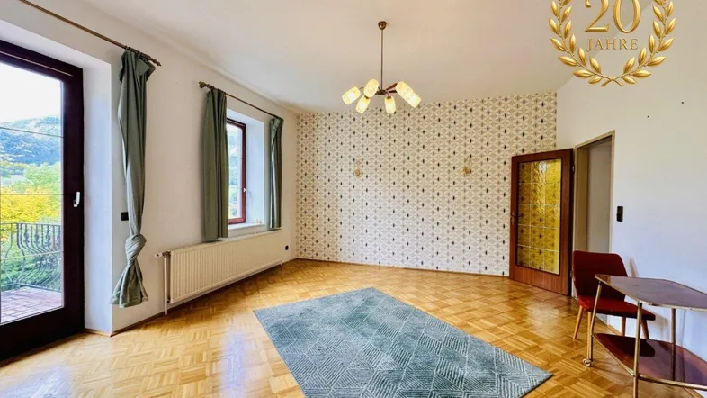 Geräumiges Wohnzimmer mit Parkettboden, gemusterter Tapete und Zugang zu einem Balkon.