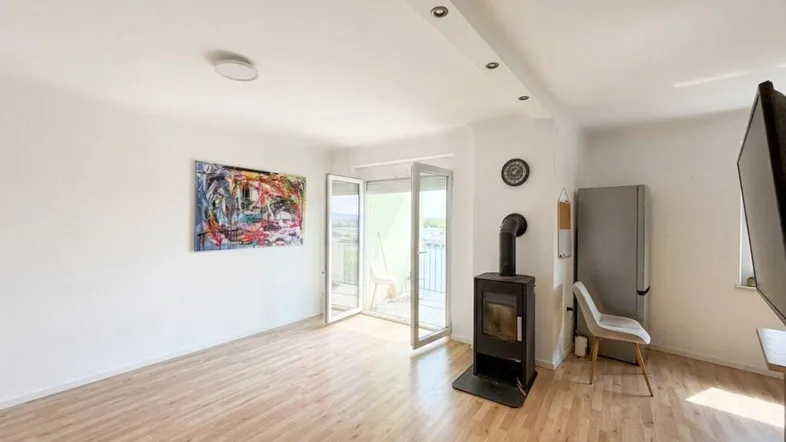 Helles Wohnzimmer mit Holzboden, modernem Kaminofen und Zugang zu einem Balkon.