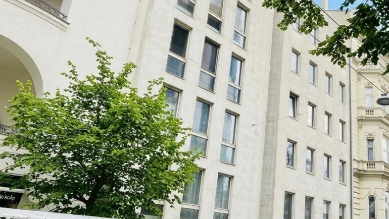 Moderne Wohngebäude-Fassade mit vielen Fenstern und Bäumen an einer städtischen Straße.