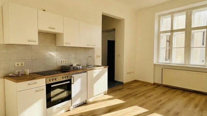 Helle, offene Küche mit weißer Einbauküche, Laminatboden und viel Tageslicht durch große Fenster.