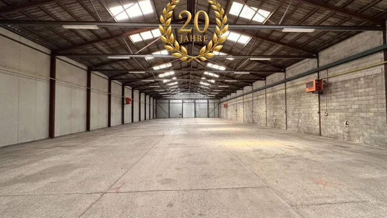 Geräumige, leere Lagerhalle mit hoher Decke, Betonboden und natürlichem Lichteinfall durch Oberlichter.