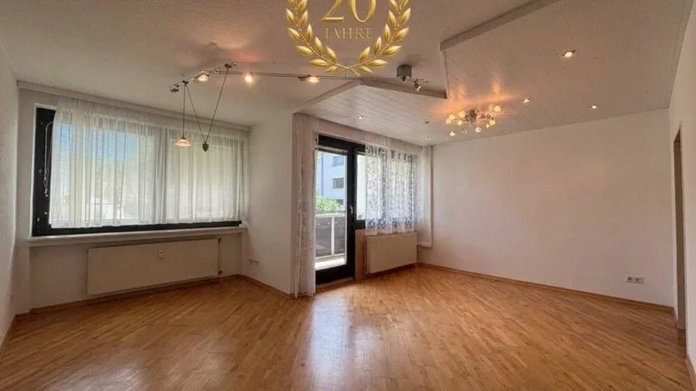 Helles Wohnzimmer mit Parkettboden, großen Fenstern und Zugang zum Balkon.