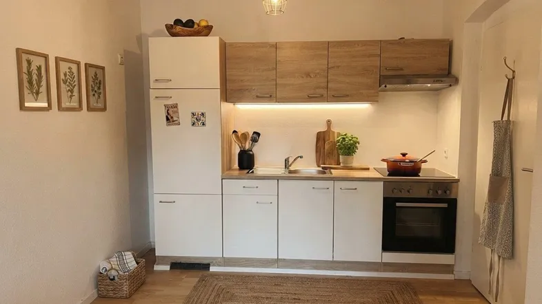 Kleine, funktionale Küche mit hellen Holz- und weißen Fronten, ausgestattet mit grundlegenden Geräten.