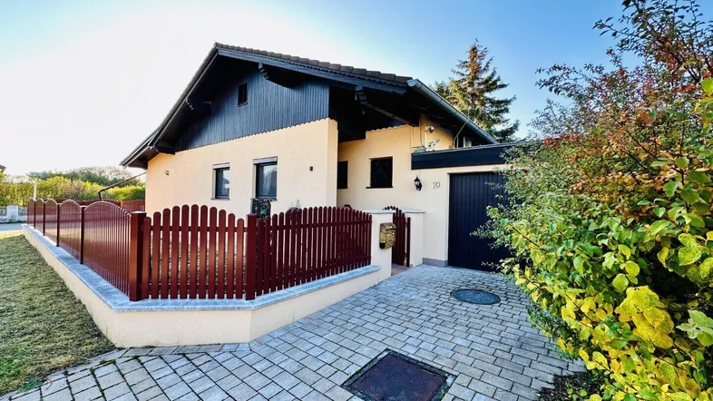 Vorderansicht des Hauses mit gepflasterter Einfahrt, Holzzaun und gepflegter Bepflanzung.