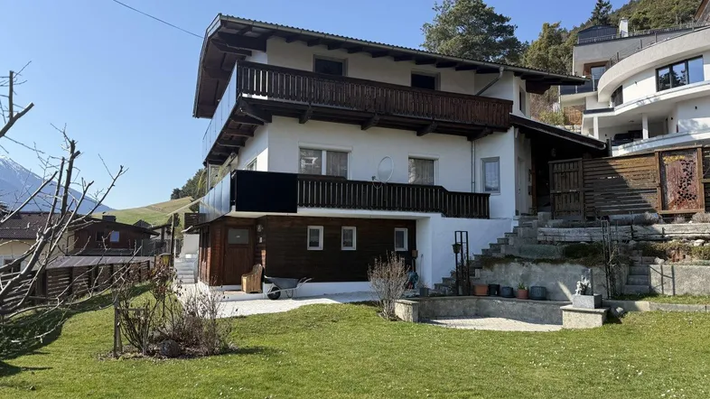 Traditionelles Haus mit mehreren Balkonen und großem Garten in alpiner Umgebung.