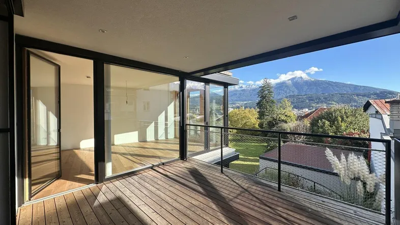 Geräumiger Balkon mit Holzboden, Glasgeländer und beeindruckendem Bergblick, direkt zugänglich vom Wohnbereich.