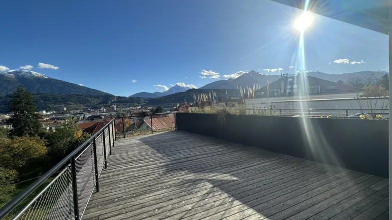 Große Holzterrasse mit weitem Blick auf die Stadt und die umliegenden Berge unter strahlendem Sonnenschein.