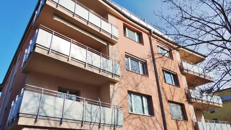 Mehrfamilienhaus mit mehreren Balkonen und einer hellen Fassade unter blauem Himmel.