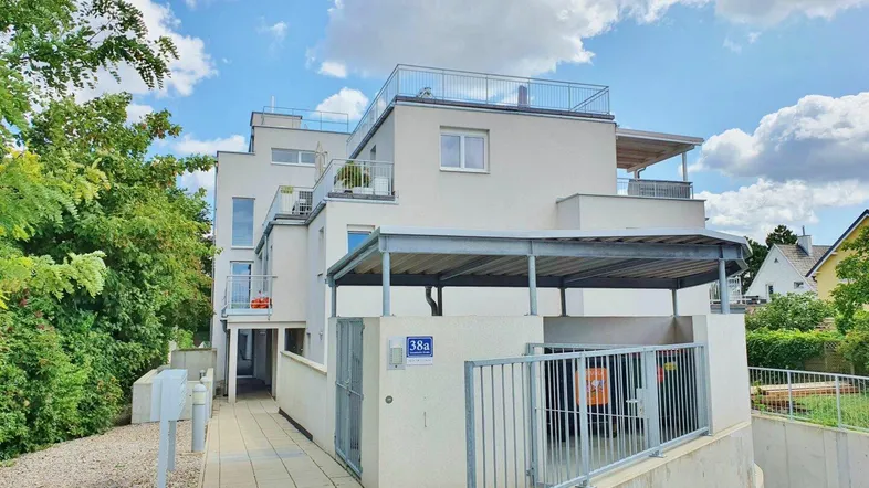 Modernes Mehrfamilienhaus mit heller Fassade, Carport und Zugang zum Eingangsbereich.