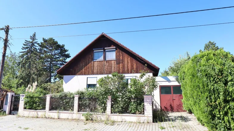 Einfamilienhaus mit Holzfassade im Obergeschoss, Vorgarten und Garagenzufahrt unter blauem Himmel.