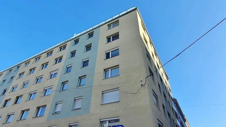 Mehrstöckiges Wohngebäude mit hellblauer und beiger Fassade unter klarem blauem Himmel.