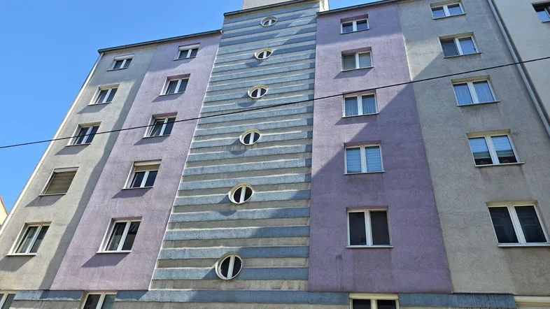 Fassade eines Mehrfamilienhauses mit ungewöhnlichen runden Fenstern und farbigen Streifen.