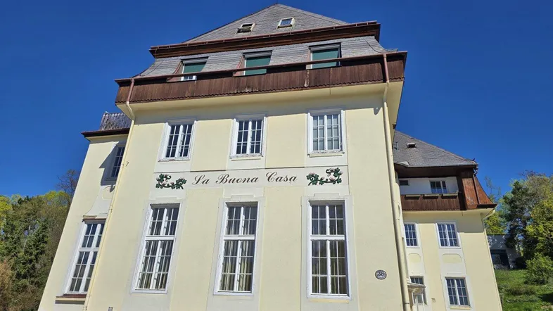 Historisches Gebäude mit gelber Fassade, Mansarddach und dekorativer Schrift.