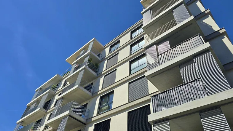 Moderne Wohngebäude-Fassade mit zahlreichen Balkonen und großen Fenstern unter blauem Himmel.