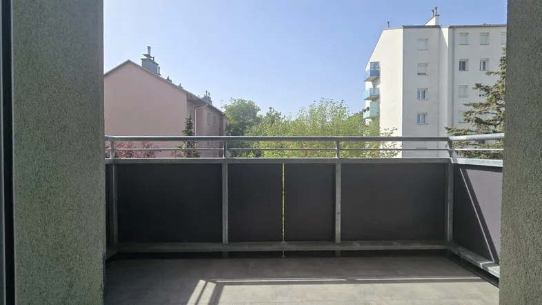 Geräumiger Balkon mit Fliesenboden und Blick auf die umliegenden Gebäude und Bäume.