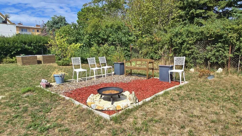 Gemütlicher Gartenbereich mit Feuerstelle und Sitzgelegenheiten, umgeben von Grünflächen und Bäumen.