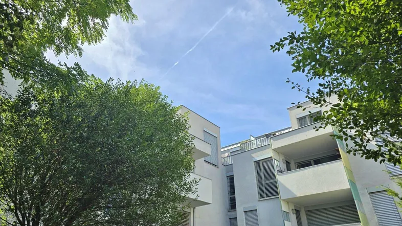Moderne Wohnanlage mit mehreren Balkonen und viel Grün unter blauem Himmel.
