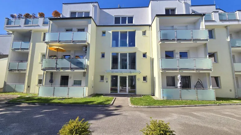 Modernes Mehrfamilienhaus mit hellgelber Fassade, vielen Balkonen und großen Fenstern unter blauem Himmel.