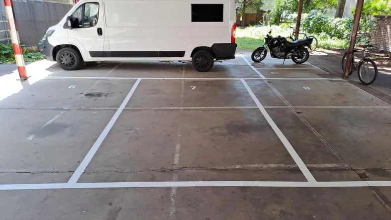 Überdachter Parkplatz mit markierten Stellflächen, einem Transporter, Motorrad und Fahrrad.