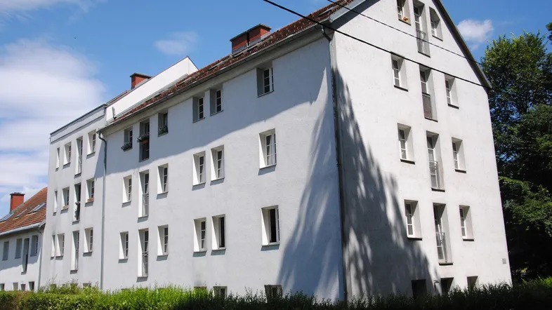 Mehrfamilienhaus mit weißer Fassade, vielen Fenstern und Satteldach unter blauem Himmel.