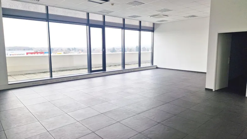 Geräumiges, leeres Büro mit großen Fenstern, die viel Tageslicht hereinlassen und einen weiten Blick bieten.