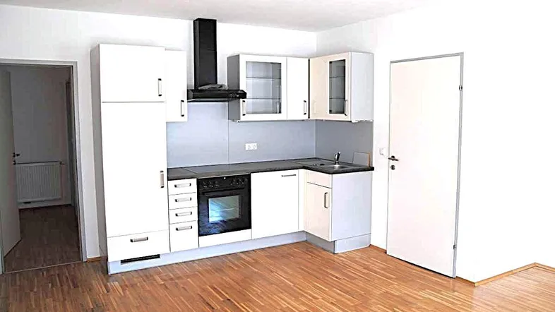 Helle Einbauküche mit weißen Schränken, integriertem Backofen und Holzparkettboden in einem offenen Raum.