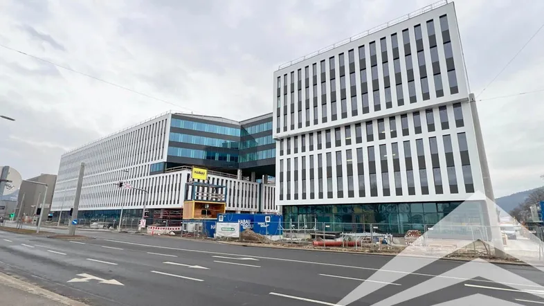 Modernes Bürogebäude mit weißer und dunkler Fassade an einer Straße unter bewölktem Himmel.