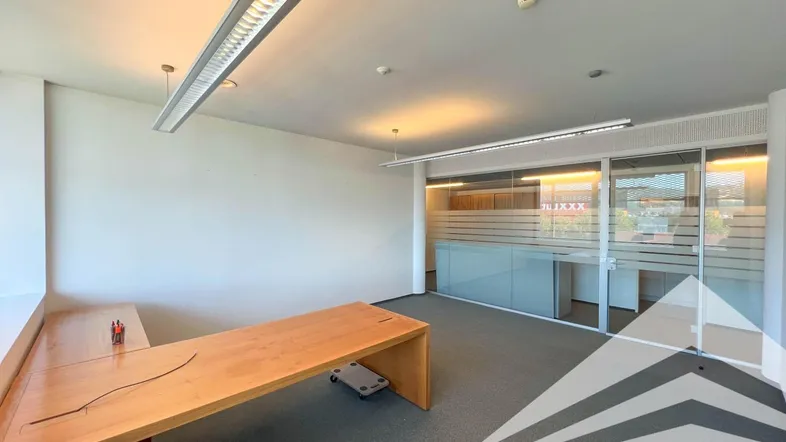 Geräumiges Büro mit modernem Holzschreibtisch, Teppichboden und Glaswänden für eine helle Arbeitsumgebung.