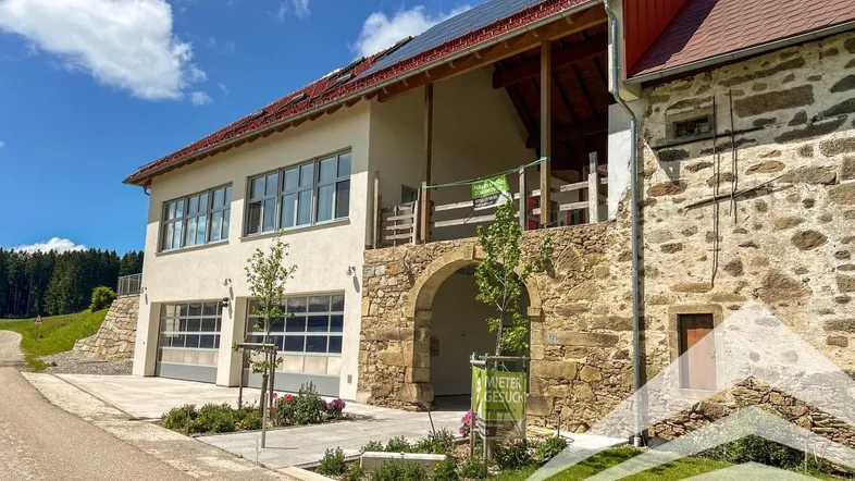 Modernes Gebäude mit traditionellen Steinelementen, Garagen und Solaranlage unter blauem Himmel.
