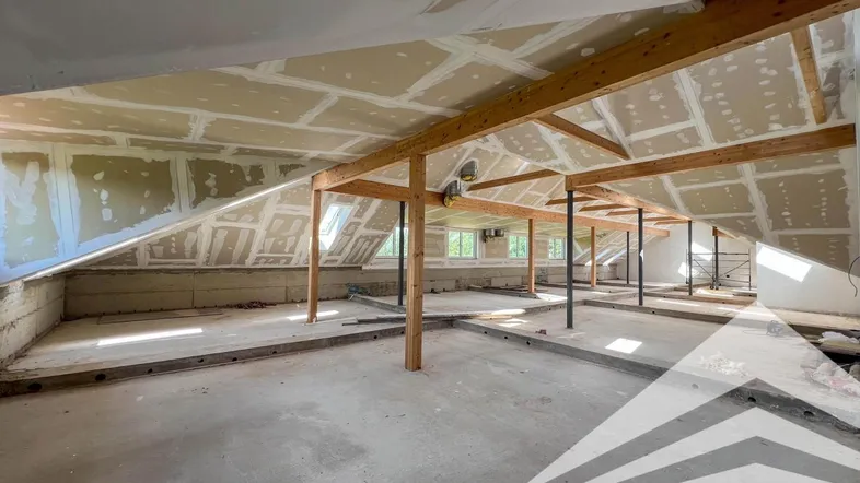 Geräumiger Dachboden im Rohbau mit sichtbaren Holzbalken und Dachschrägen, bereit für den Ausbau.