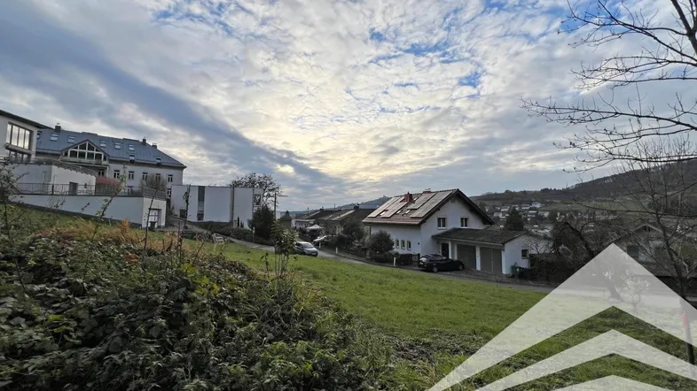 Blick auf eine Wohnsiedlung mit Häusern, grünen Hügeln und einem bewölkten Himmel.